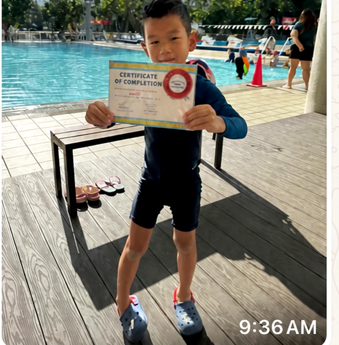 Penguin Swim School learner holding a swimming assessment completion certificate after coaching support