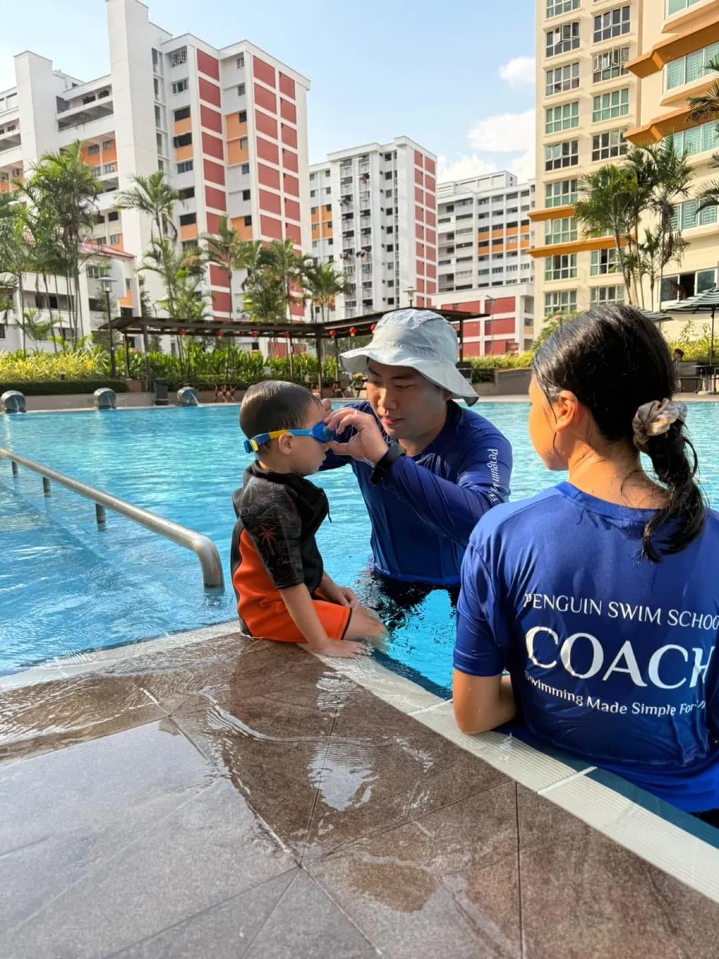 Two Penguin Swim School coaches helping a young child prepare for a private condo-pool lesson