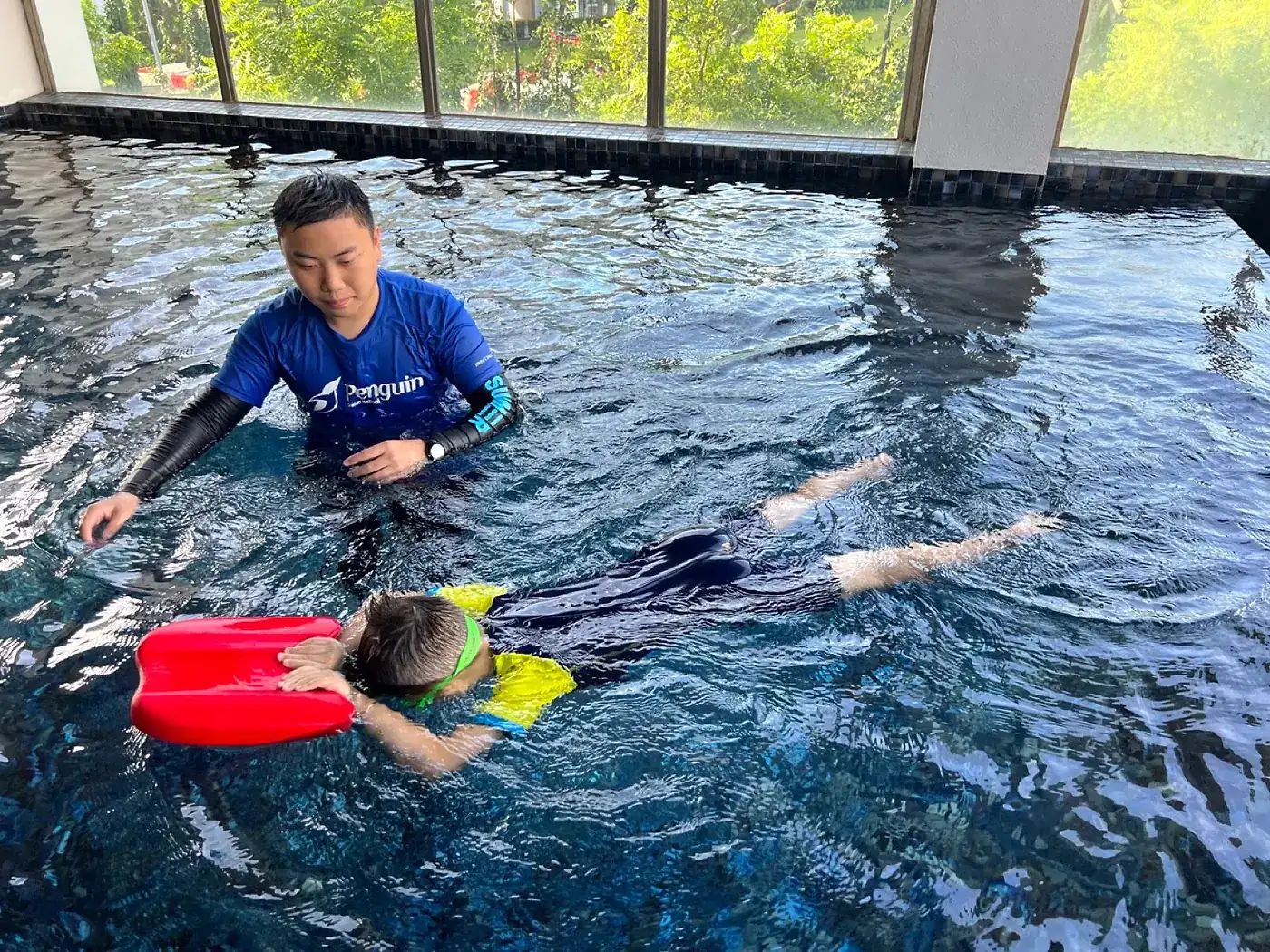 Rayner Teo coaching a child with a kickboard during a Penguin Swim School private kids swimming lesson