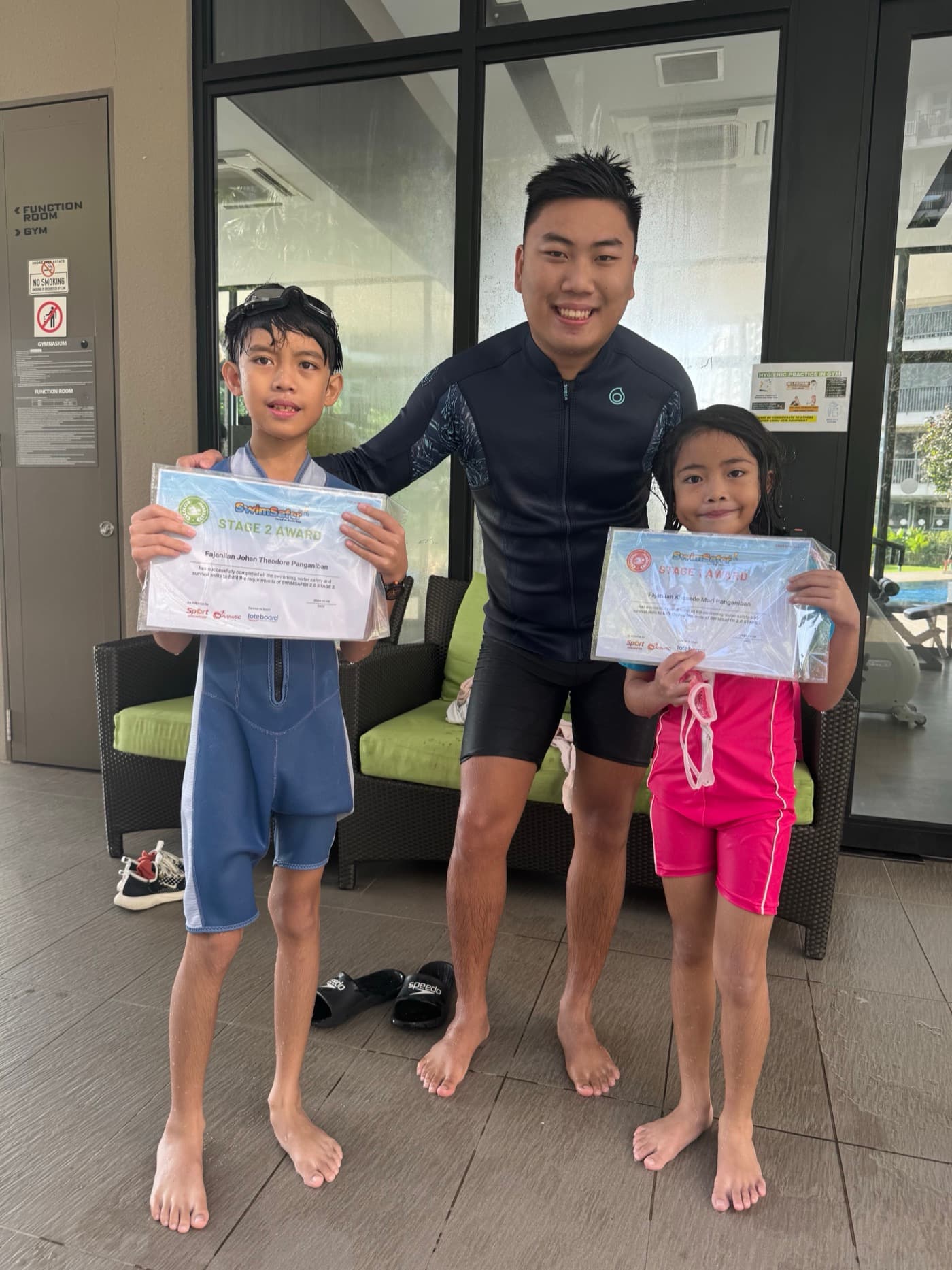 Coach Rayner with two Penguin Swim School learners holding SwimSafer Stage 1 and Stage 2 certificates