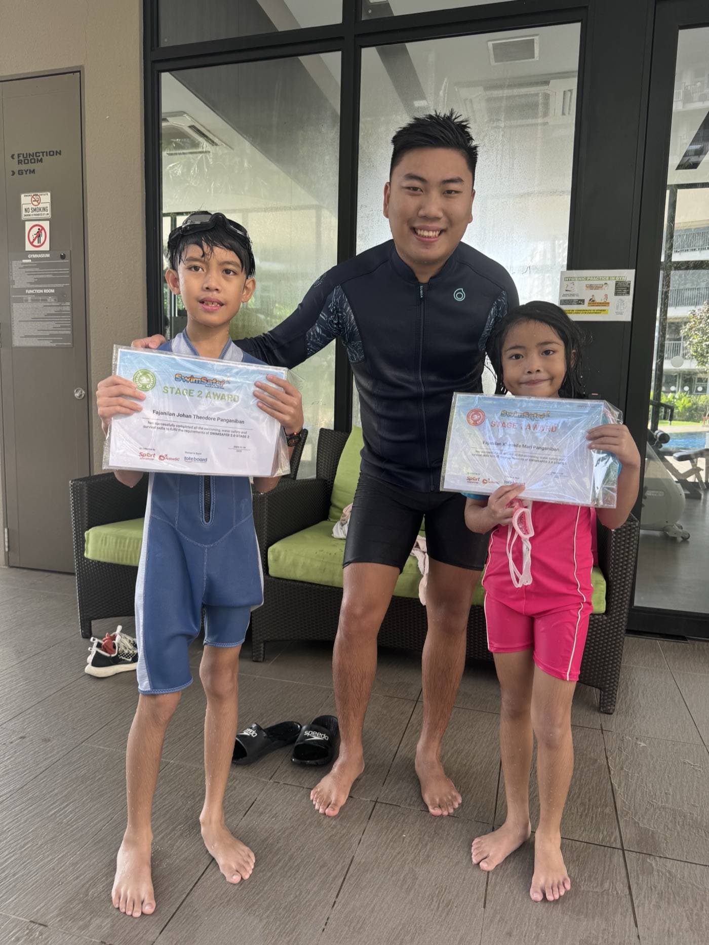 Coach Rayner with two Penguin Swim School learners holding SwimSafer Stage 1 and Stage 2 certificates