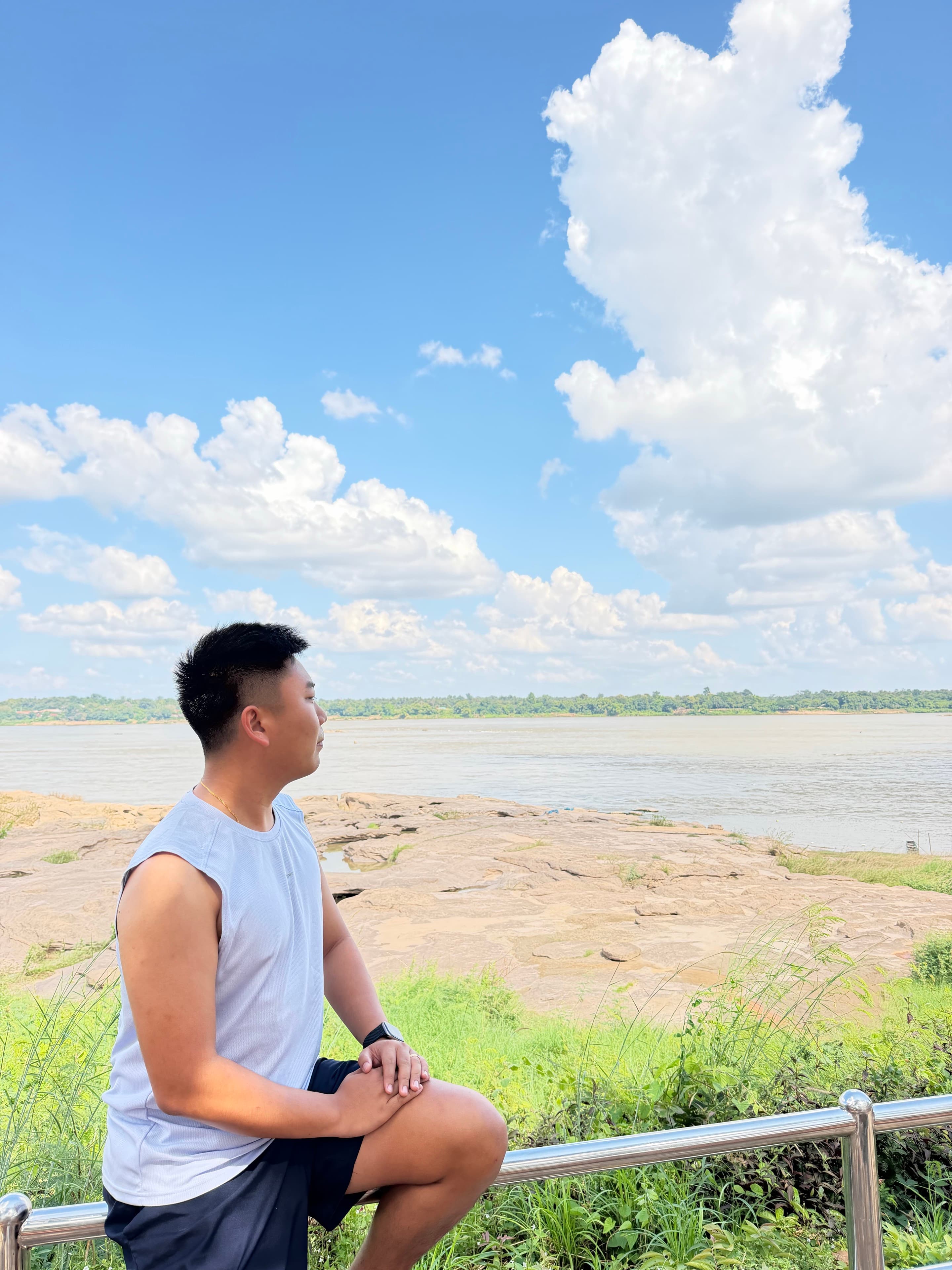 Rayner Teo seated beside a river beneath a bright blue sky